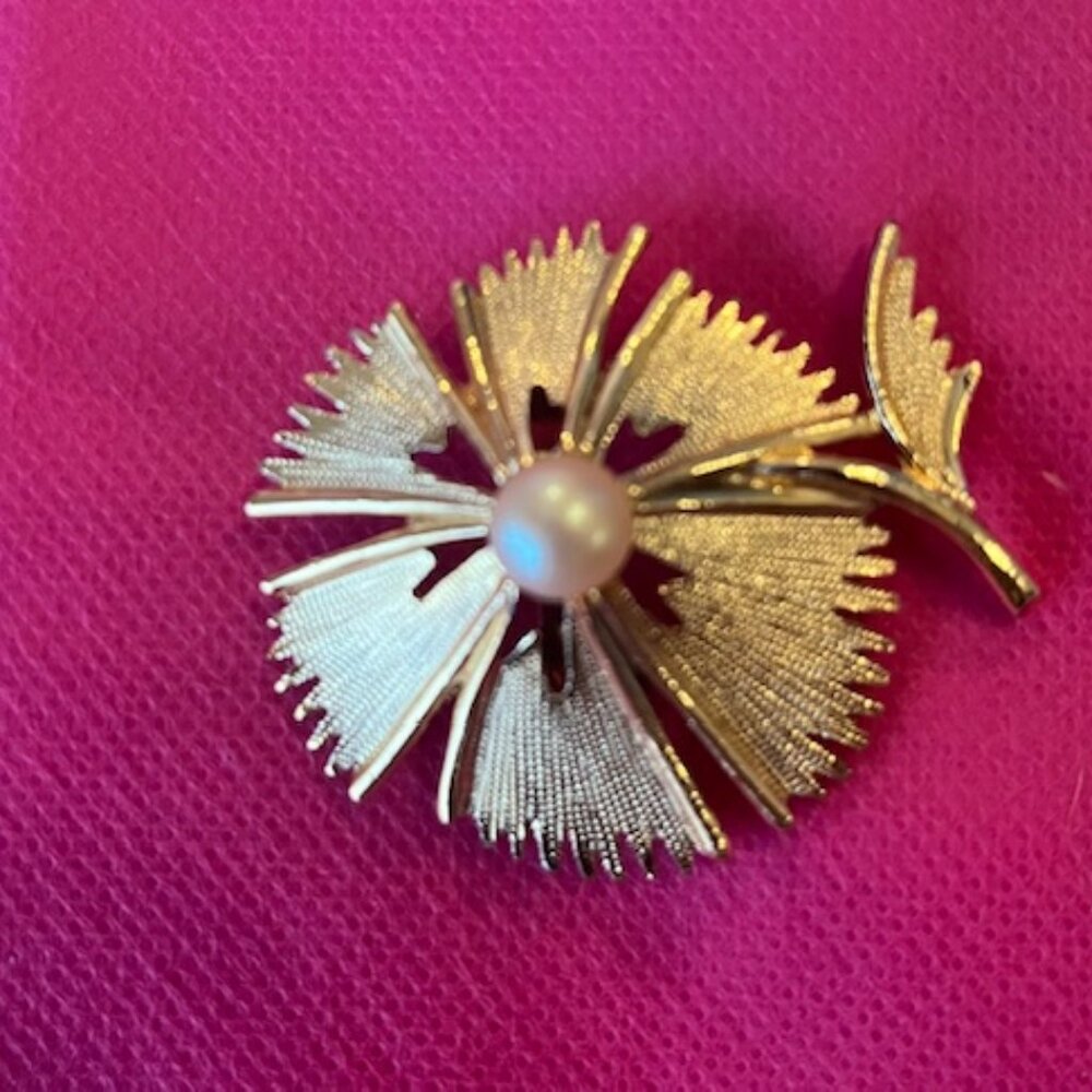A gold-tone abstract flower brooch with a faux pearl center.